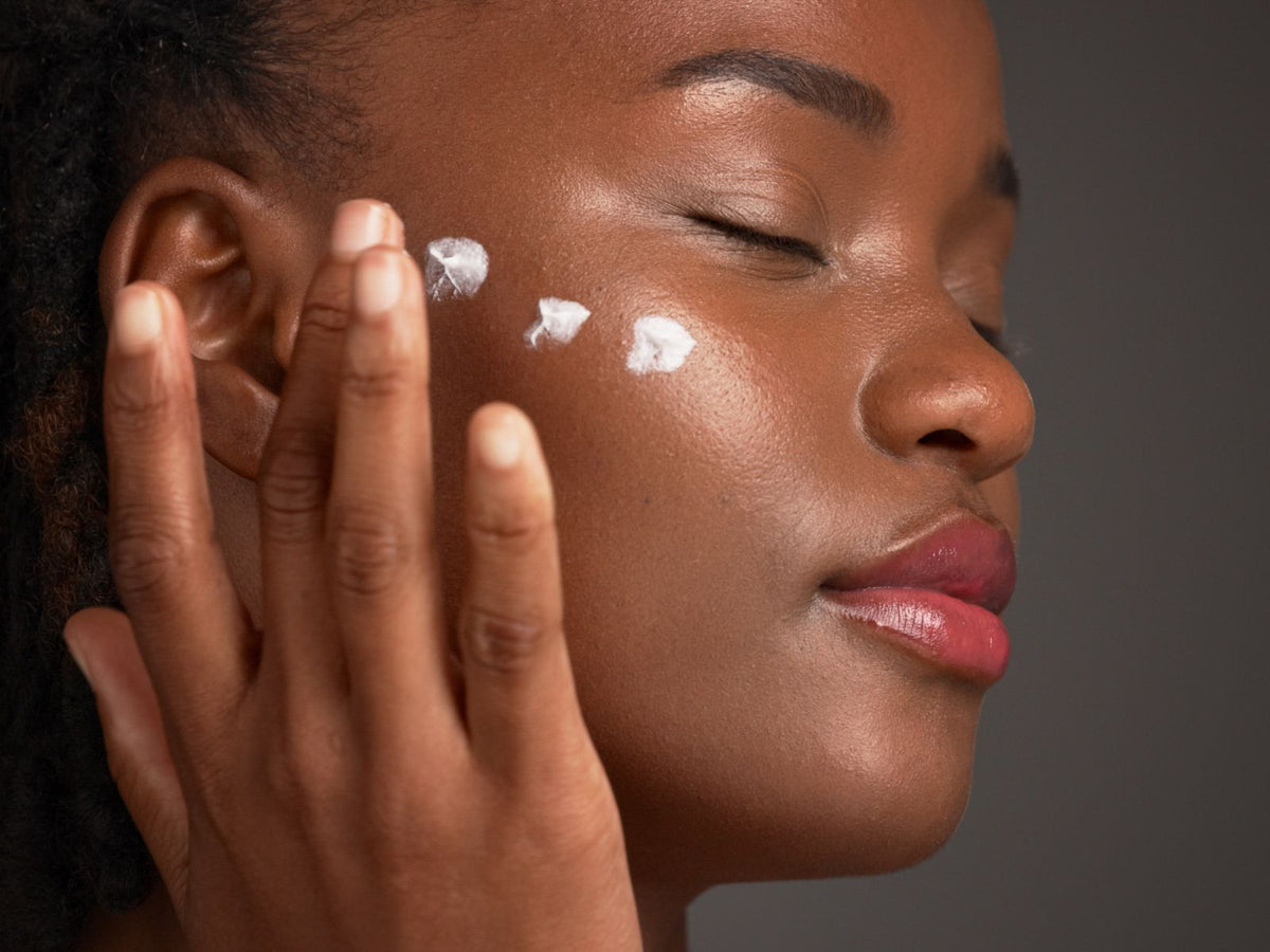 Femme noire appliquant une crème hydratante sur son visage pour une peau douce et lumineuse